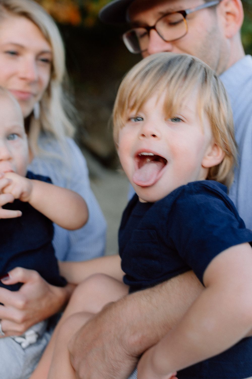 Cheerful toddler boy sticking out tongue during a fun outdoor family photo session.