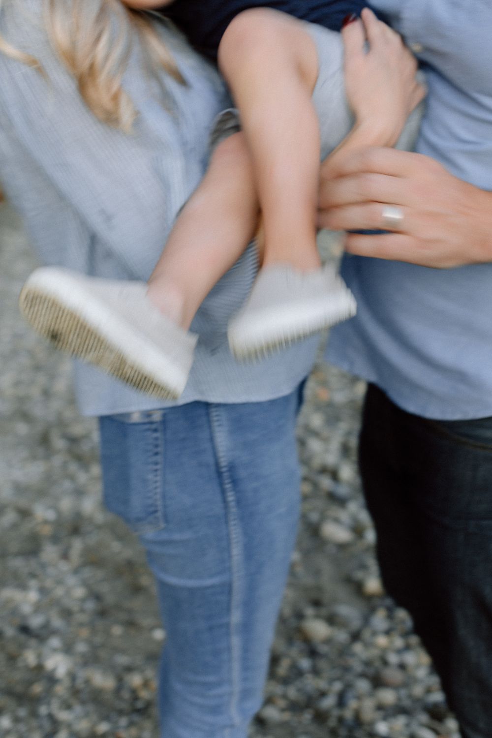 Blurred close-up of a child's white sneakers being held by parents outdoors.