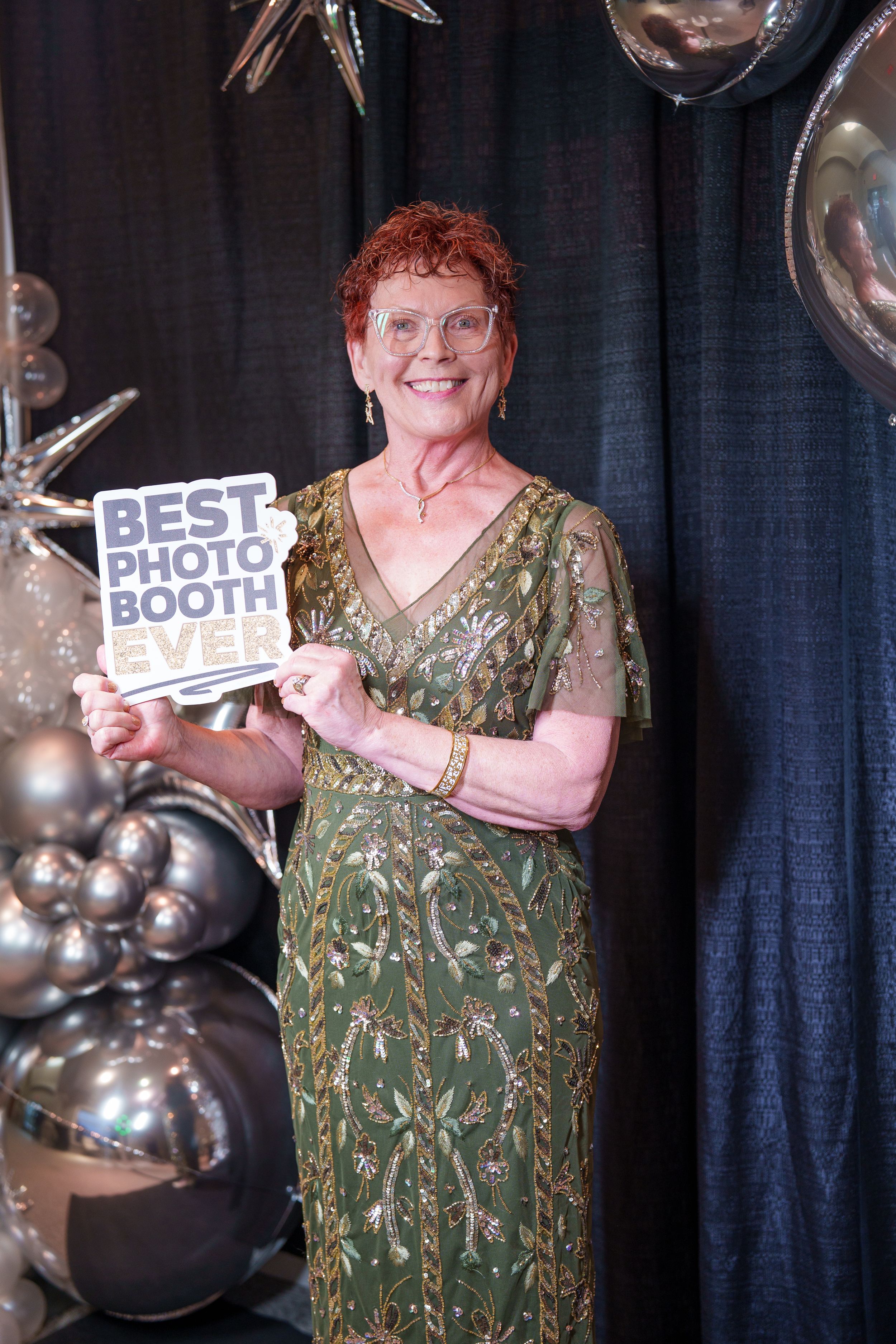 Four connected photos show someone in a green patterned dress posing with silver balloon decorations and signs at an event.