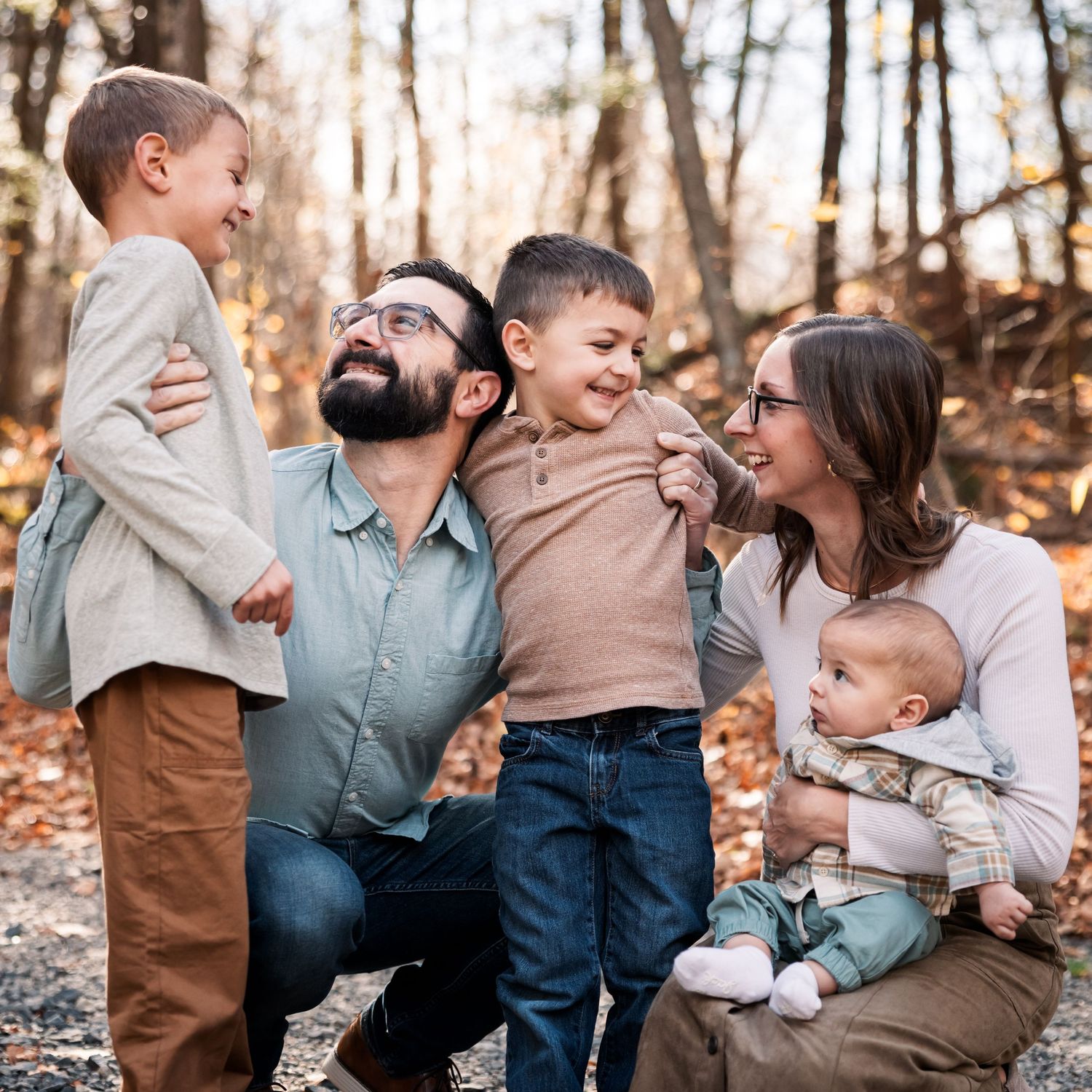 A happy family of five enjoys an autumn outdoor portrait among fall foliage, with parents and three young children smiling.