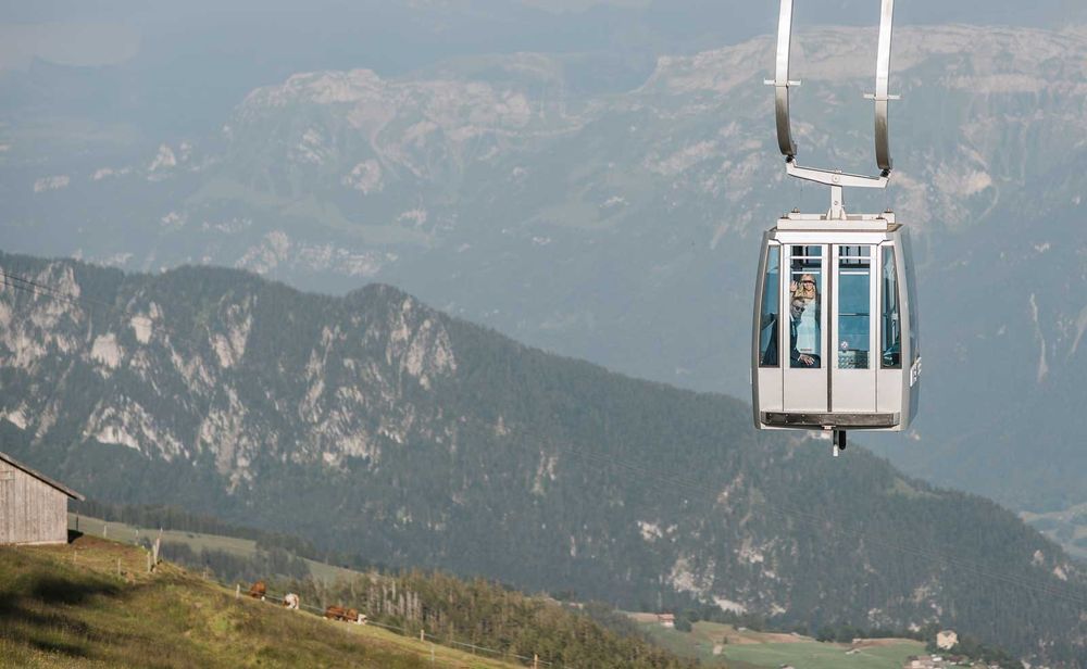 A cable car gondola suspended high above a scenic alpine mountain landscape on a clear day.