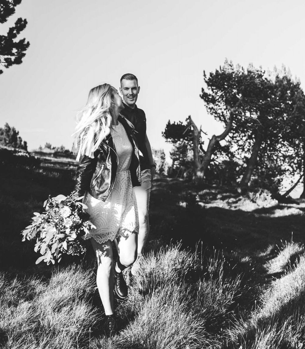 Black and white photo of couple laughing together on windswept mountain hillside with pine trees.