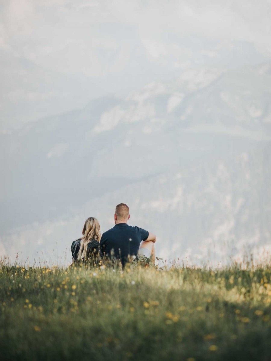 Couple sitting together in a wildflower meadow gazing at misty mountain views on a peaceful summer day.