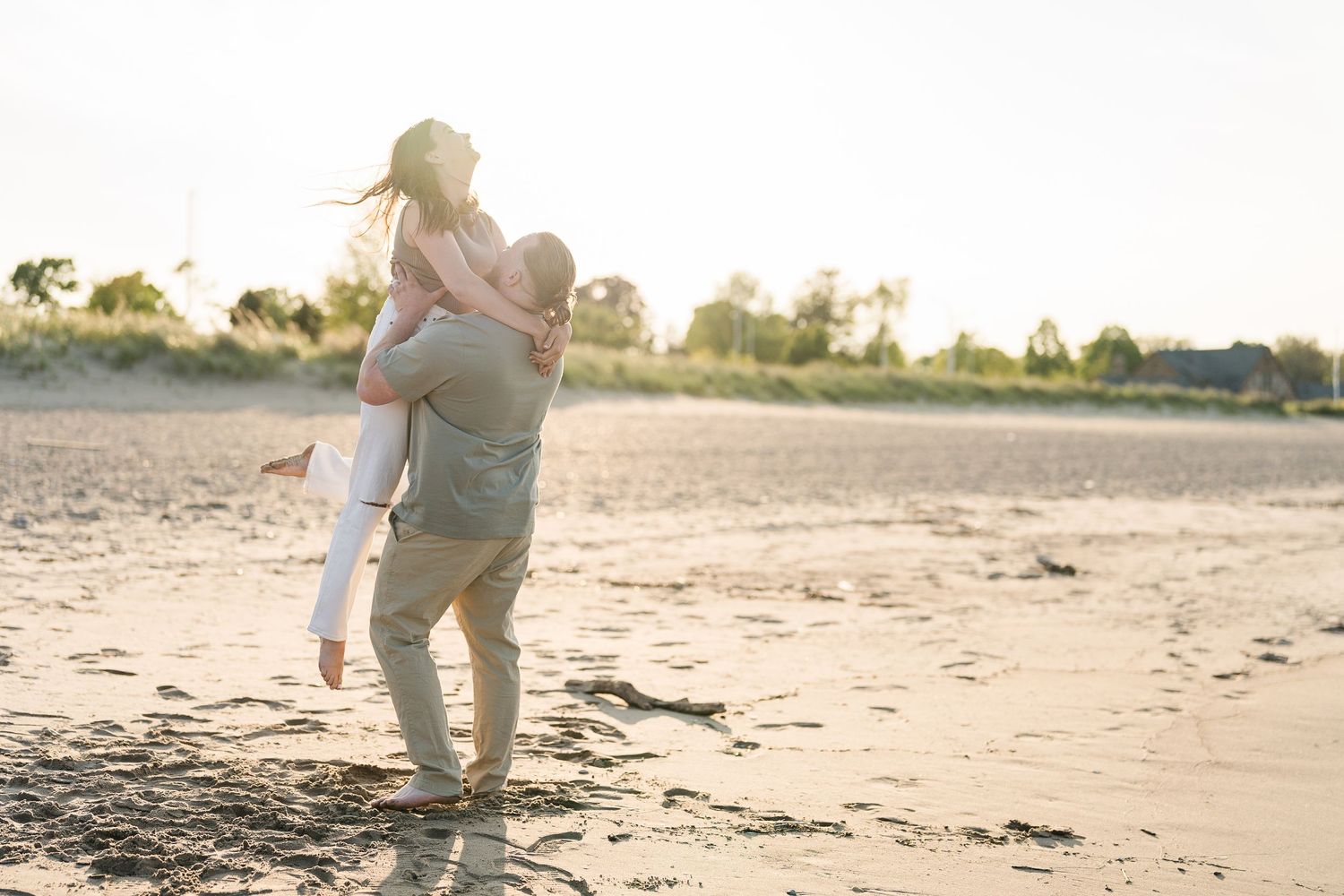 Couple sharing a joyful moment on a sandy beach at golden hour, man lifting woman.