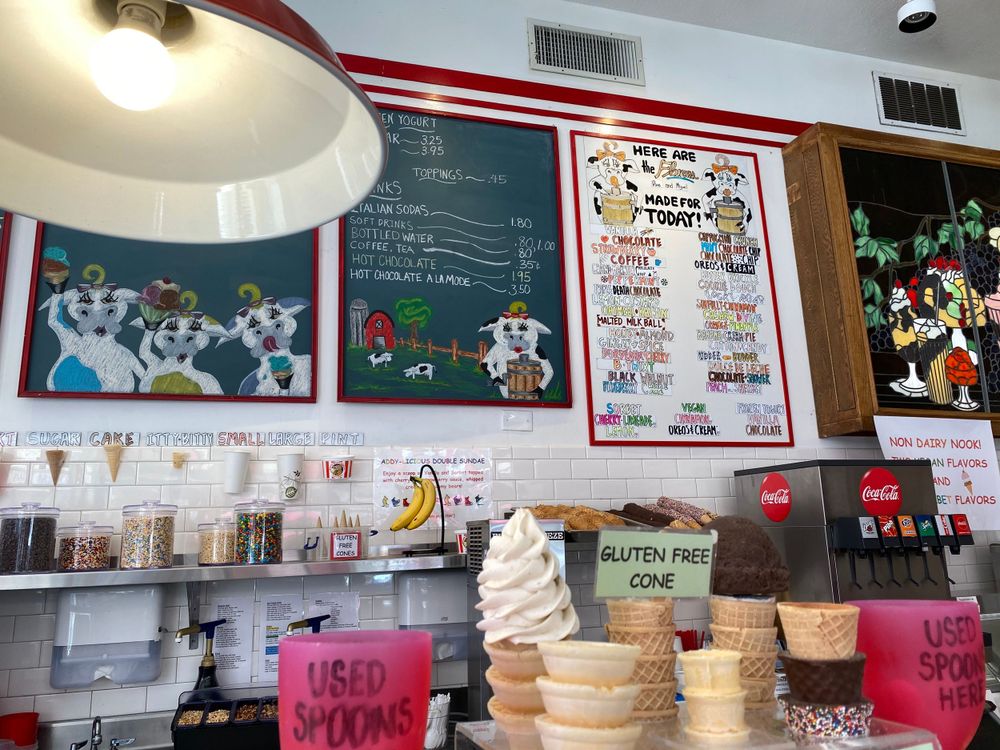 Ice cream shop menu board and counter display with soft serve cones and toppings.