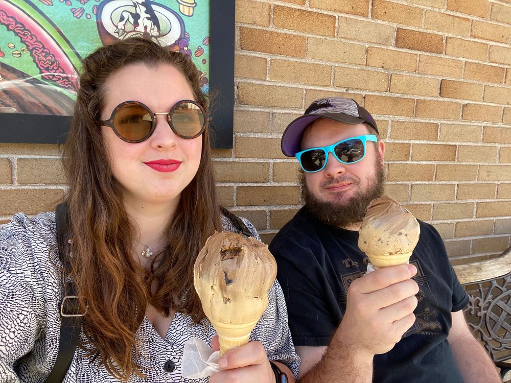 Couple enjoying ice cream cones while sitting outside a brick building.