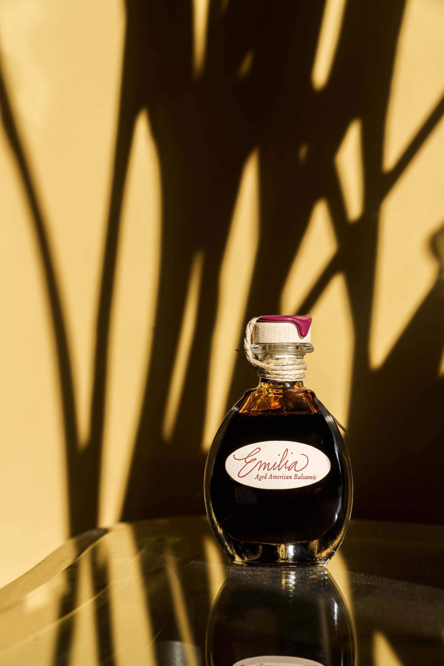 Decorative glass bottle of Emilia's liqueur casting dramatic shadows against a beige wall.