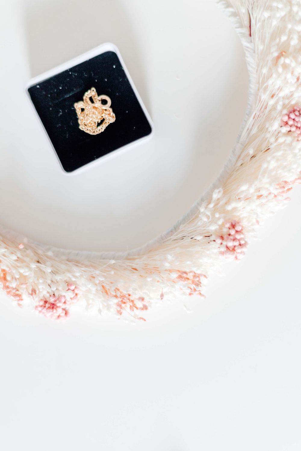 Gold charm displayed in black box with delicate pink floral accents.