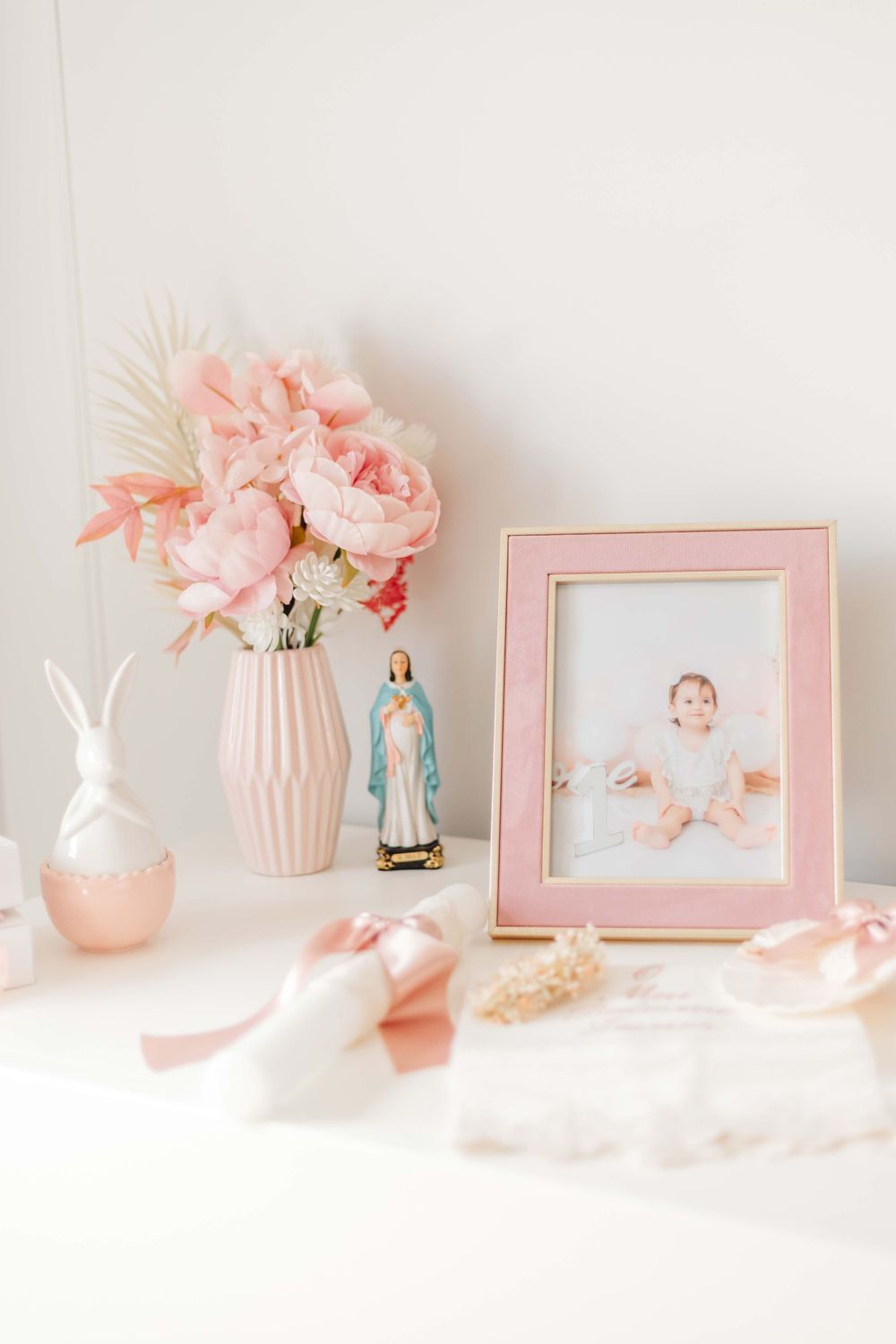 Pink roses in a vase with religious figurine and frame on white surface with delicate decorations.