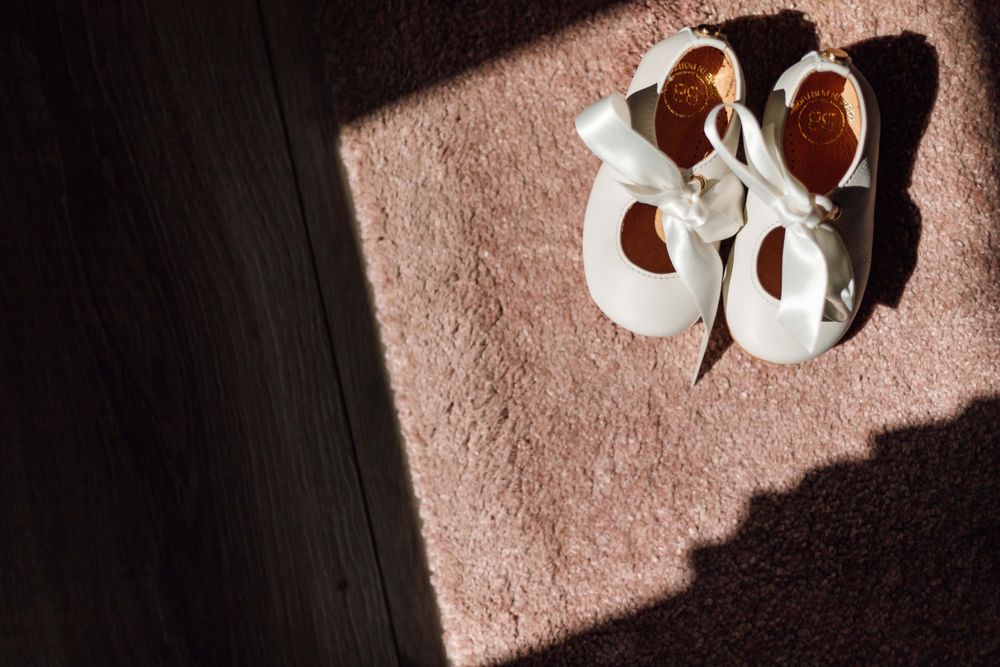 White baby shoes cast shadows on a pink carpeted floor.