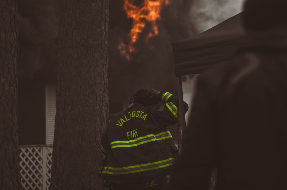 Valdosta firefighter in reflective gear works near a burning building at night.