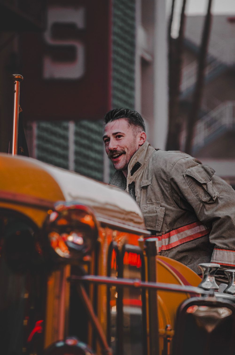 Person in tan jacket smiling while leaning on yellow machinery outdoors.