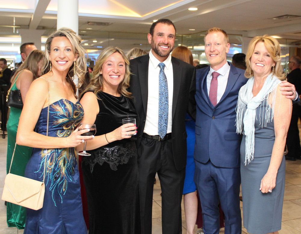 A group of five people in formal attire pose together at an elegant event.