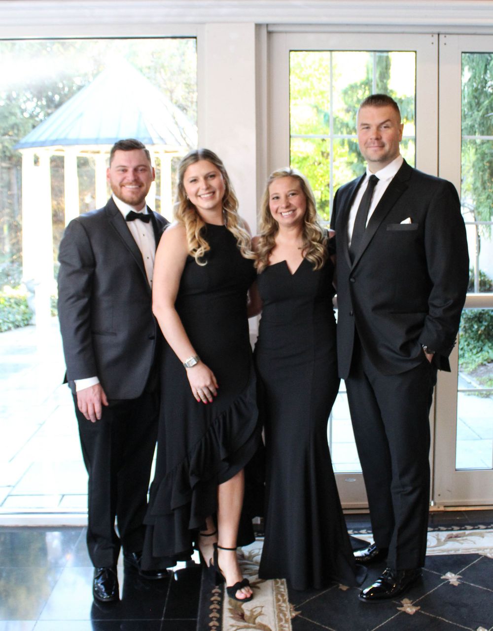 Four formally dressed attendees in black attire pose together at an elegant venue.