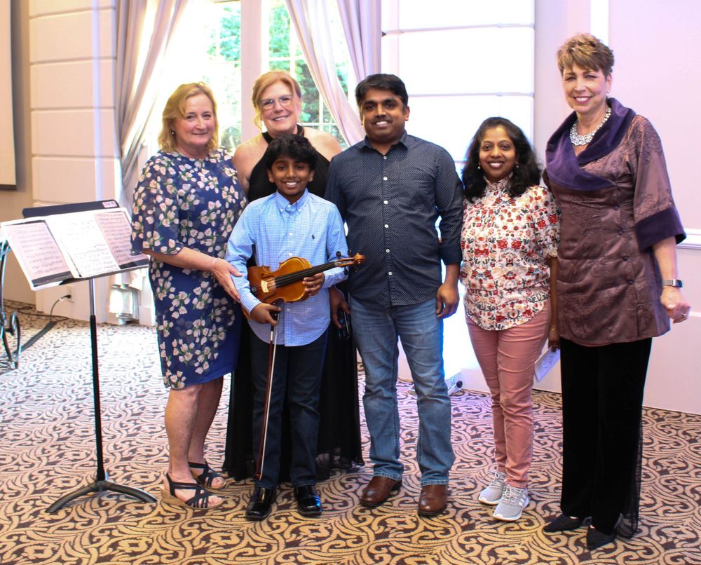 A group poses together with a young musician holding a violin at a musical performance.