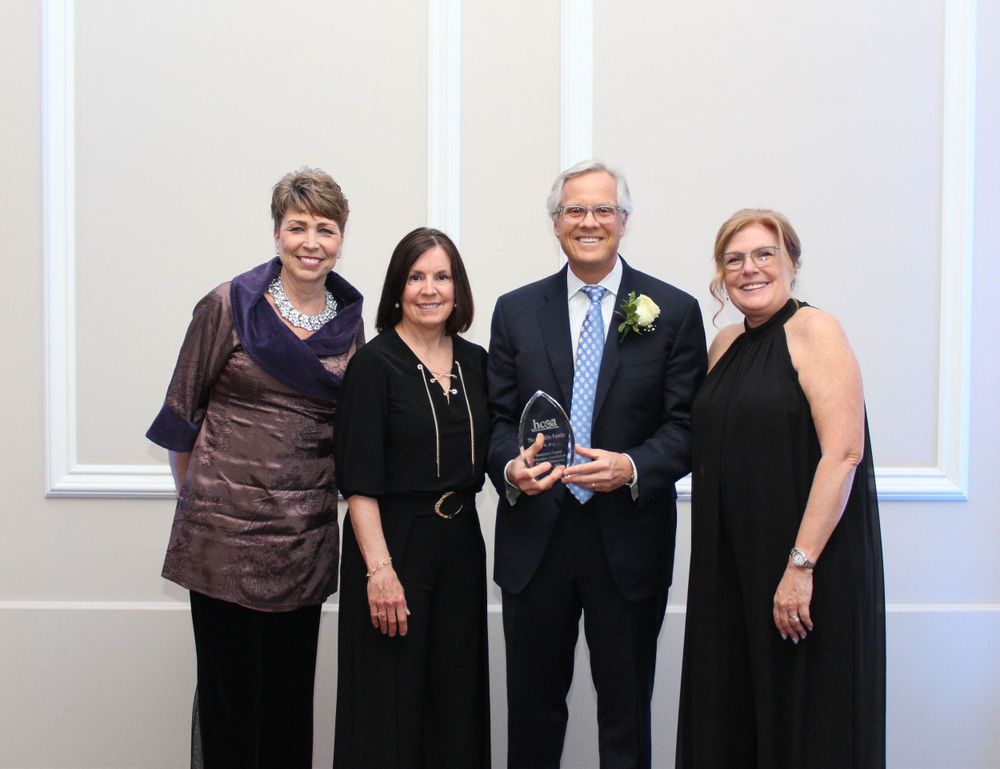 Four people in formal attire pose with an award trophy at an evening event.