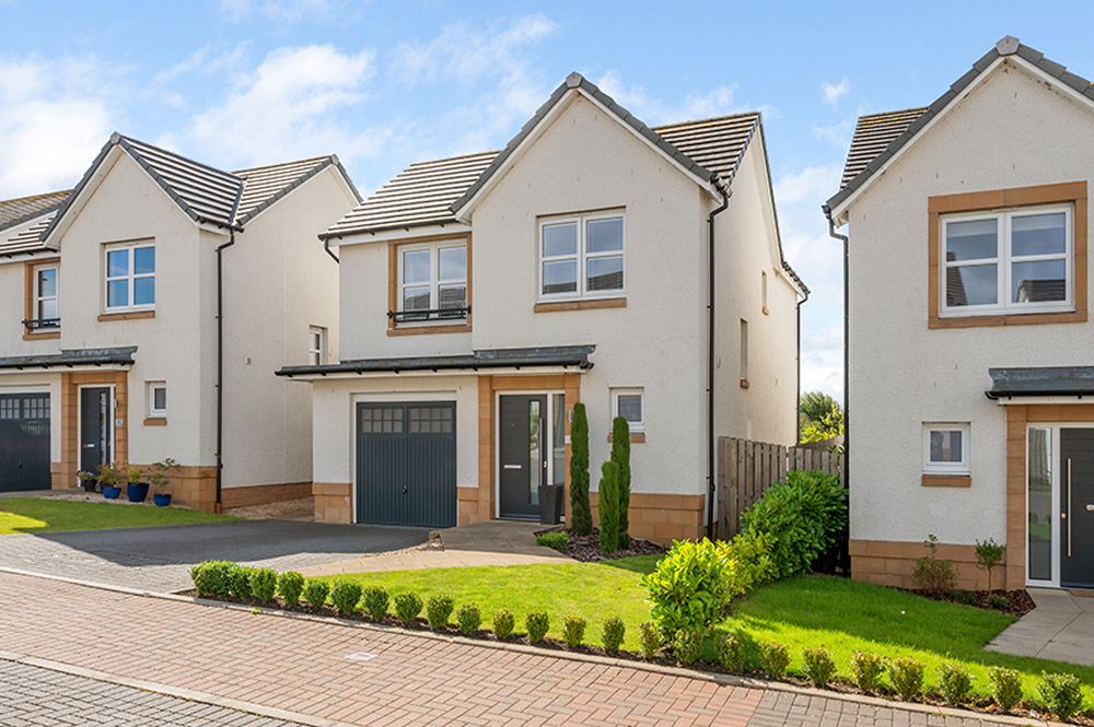 Modern detached house with gray garage door and manicured front lawn in a residential development.