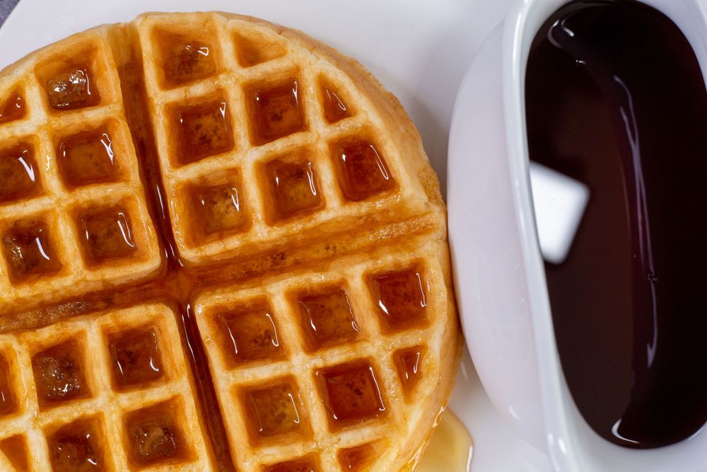 Close-up of perfectly cooked waffle with syrup and chocolate sauce.