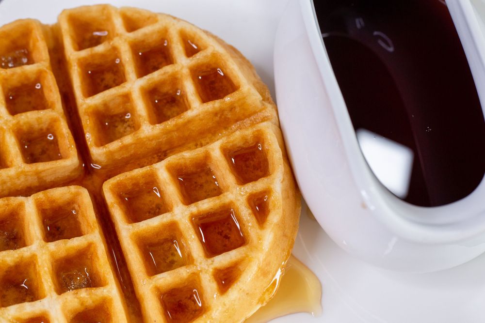 Golden waffle with syrup and dark chocolate sauce in white dish.