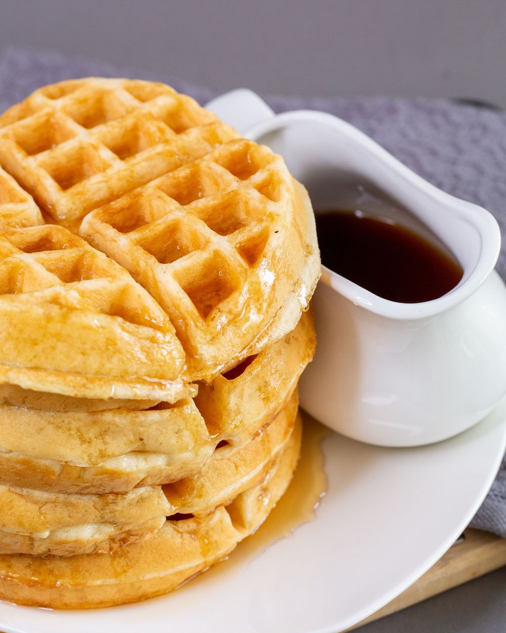 Stack of golden waffles served with maple syrup in white ceramic dish.