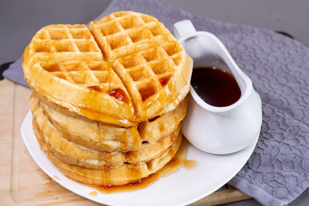 Stack of crispy waffles with syrup on gray textured placemat.