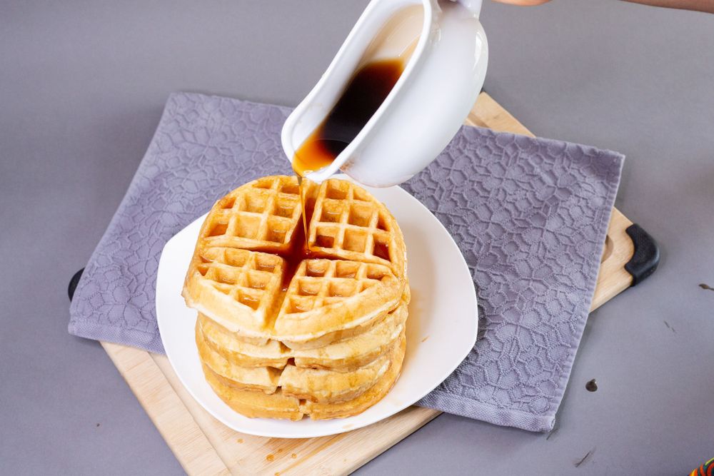 Stack of waffles being drizzled with syrup on a purple napkin.