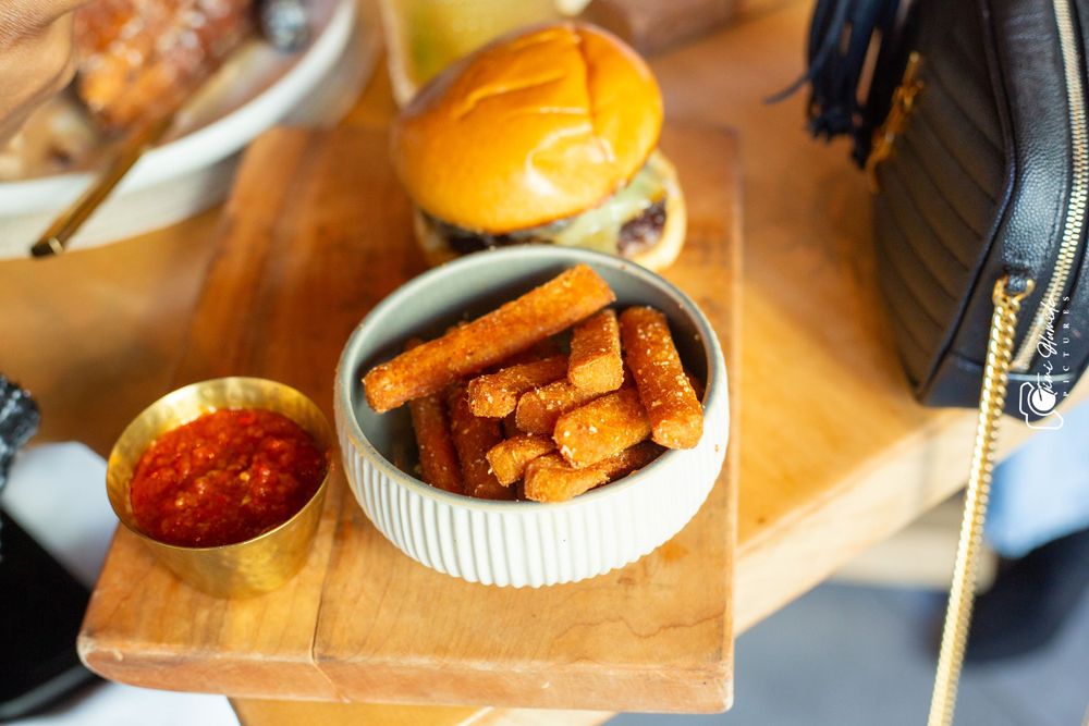 A wooden serving board with french fries and dipping sauce next to an orange.