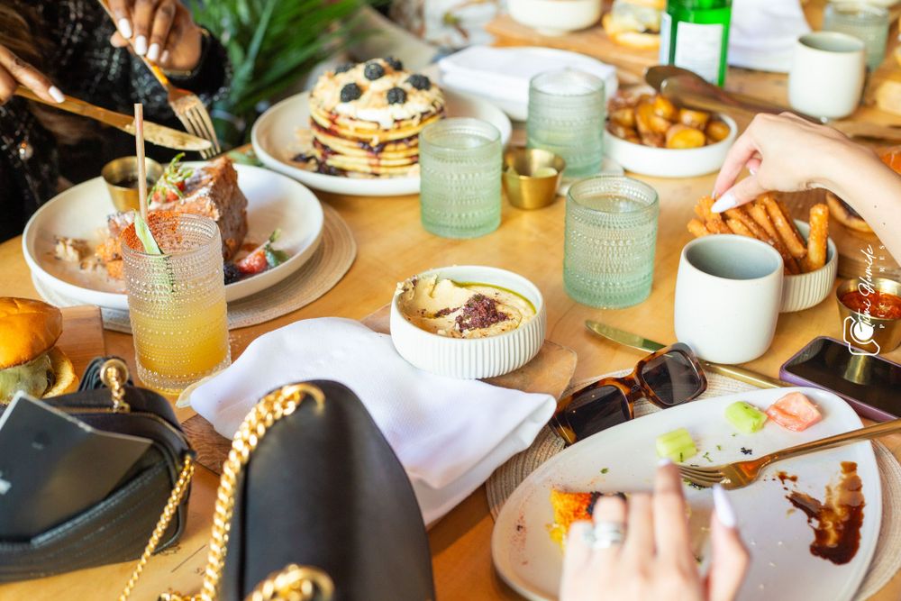 Brunch table spread with pancakes, drinks in mason jars, and coffee cups on a wooden surface.
