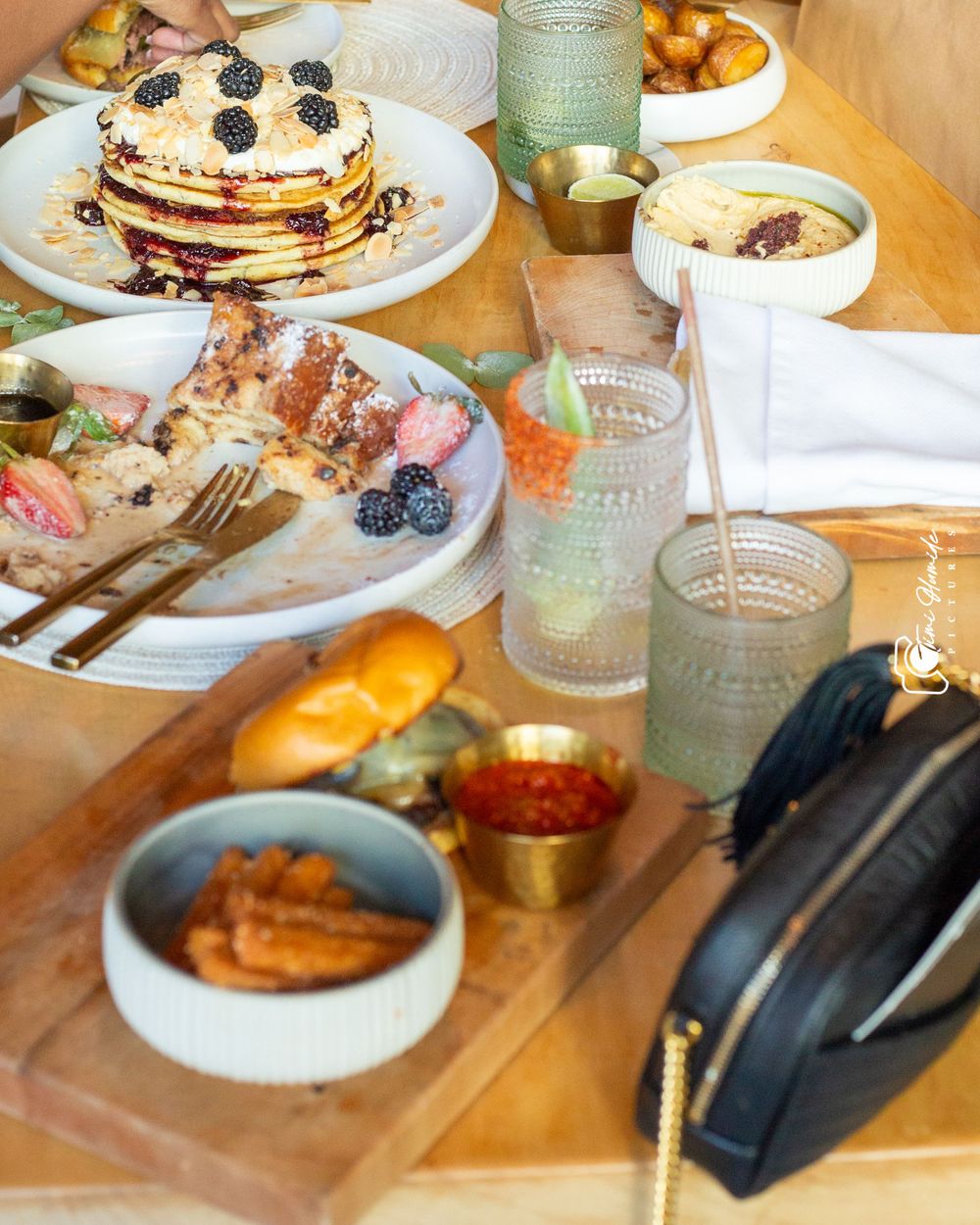 Stack of berry pancakes with sides and beverages on a rustic wooden dining table.