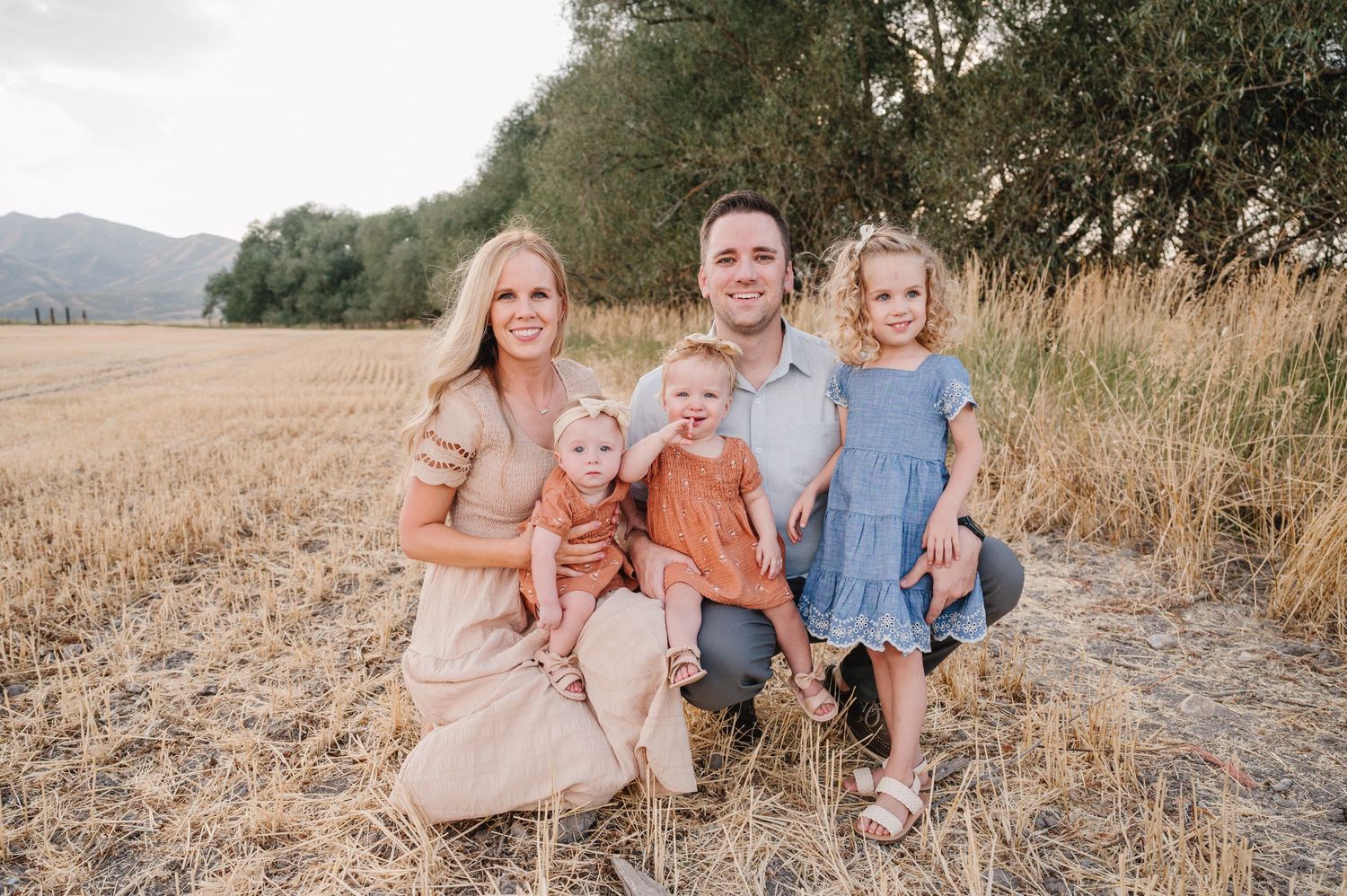 A family portrait taken in a rustic outdoor setting with mountains and dry grass.
