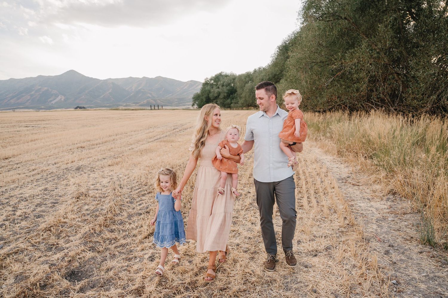 A family walking together along a dirt path with mountains and fields in the background.