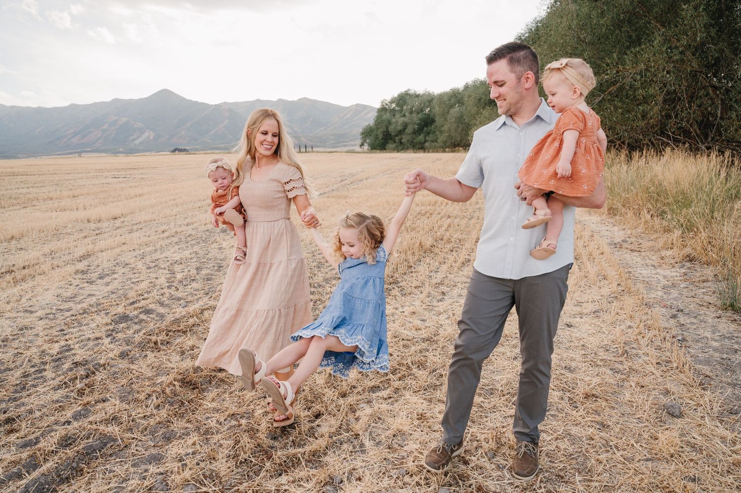 A family enjoying time together in a golden field with mountains in the distance.