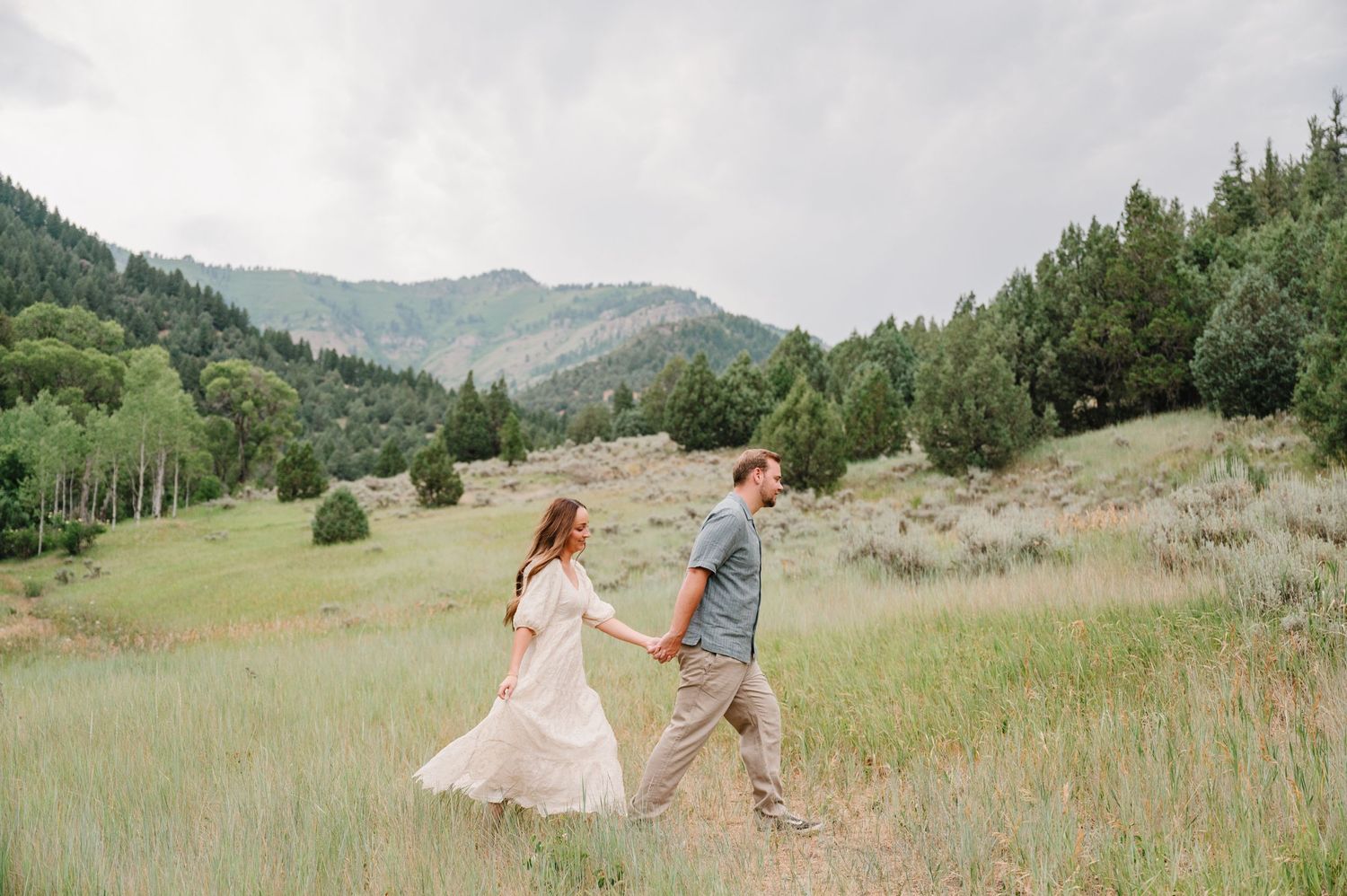 A couple holding hands while walking through a wildflower-filled mountain meadow.