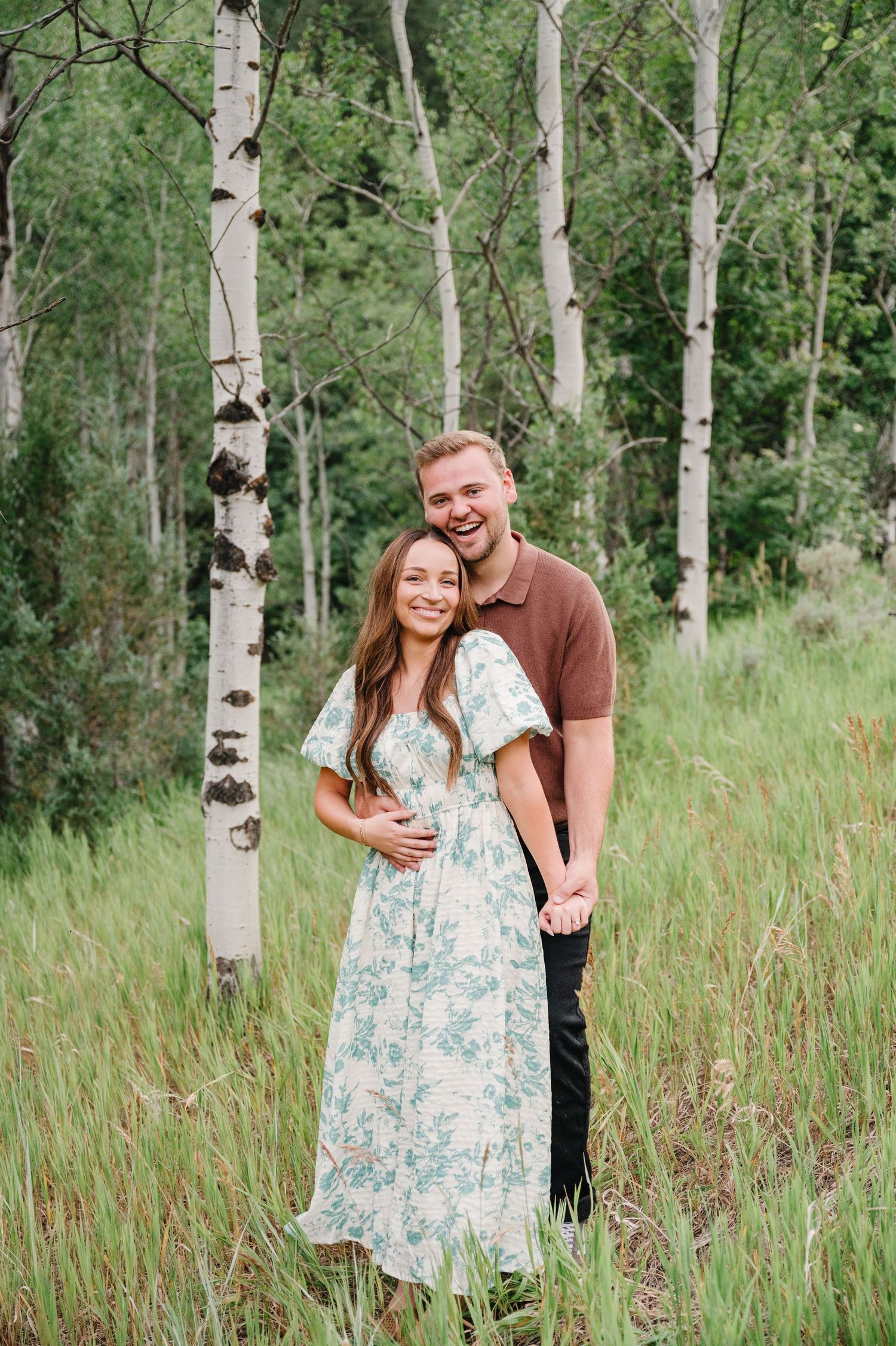 A couple sharing a joyful moment among white birch trees in a lush summer meadow.