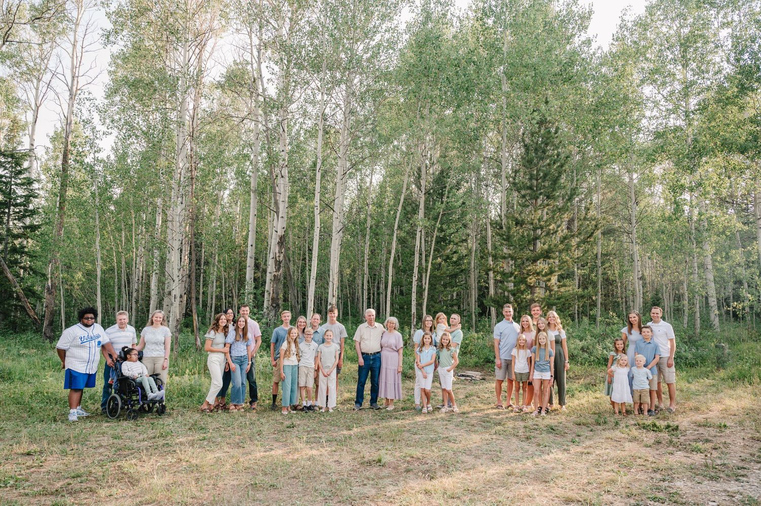Large group photo with mountain backdrop among aspen trees on a sunny day.