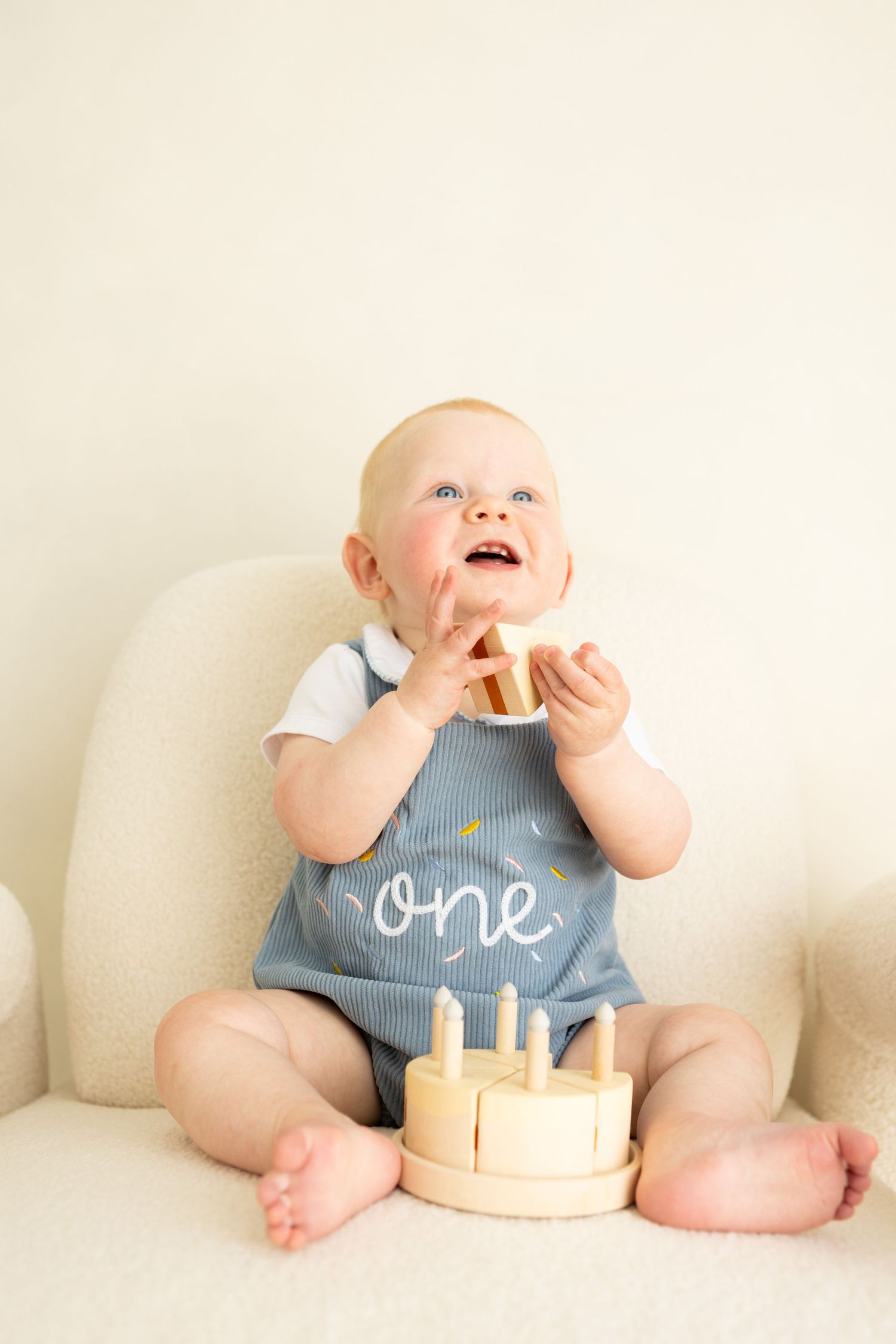 baby boy celebrating his 1st birthday in his milestone studio session holding wooden cake
