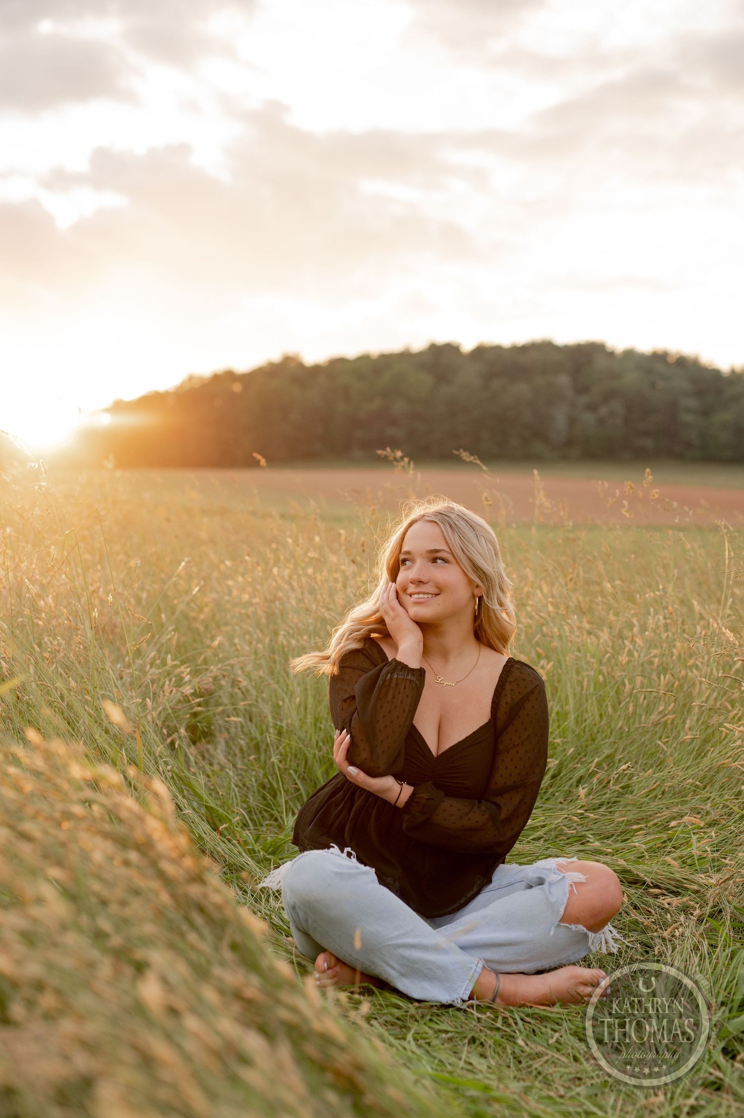 Peaceful sunset portrait sitting cross-legged in a field of tall grass.