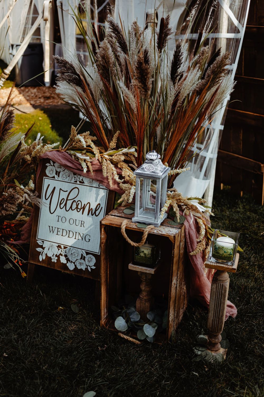 Rustic wedding welcome sign display with dried pampas grass and vintage lantern decor.