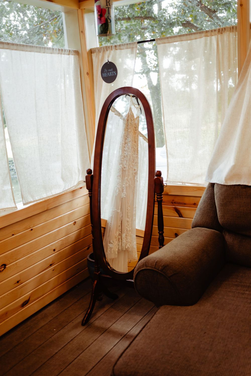 A wedding dress reflection in a full-length mirror in a wood-paneled room.