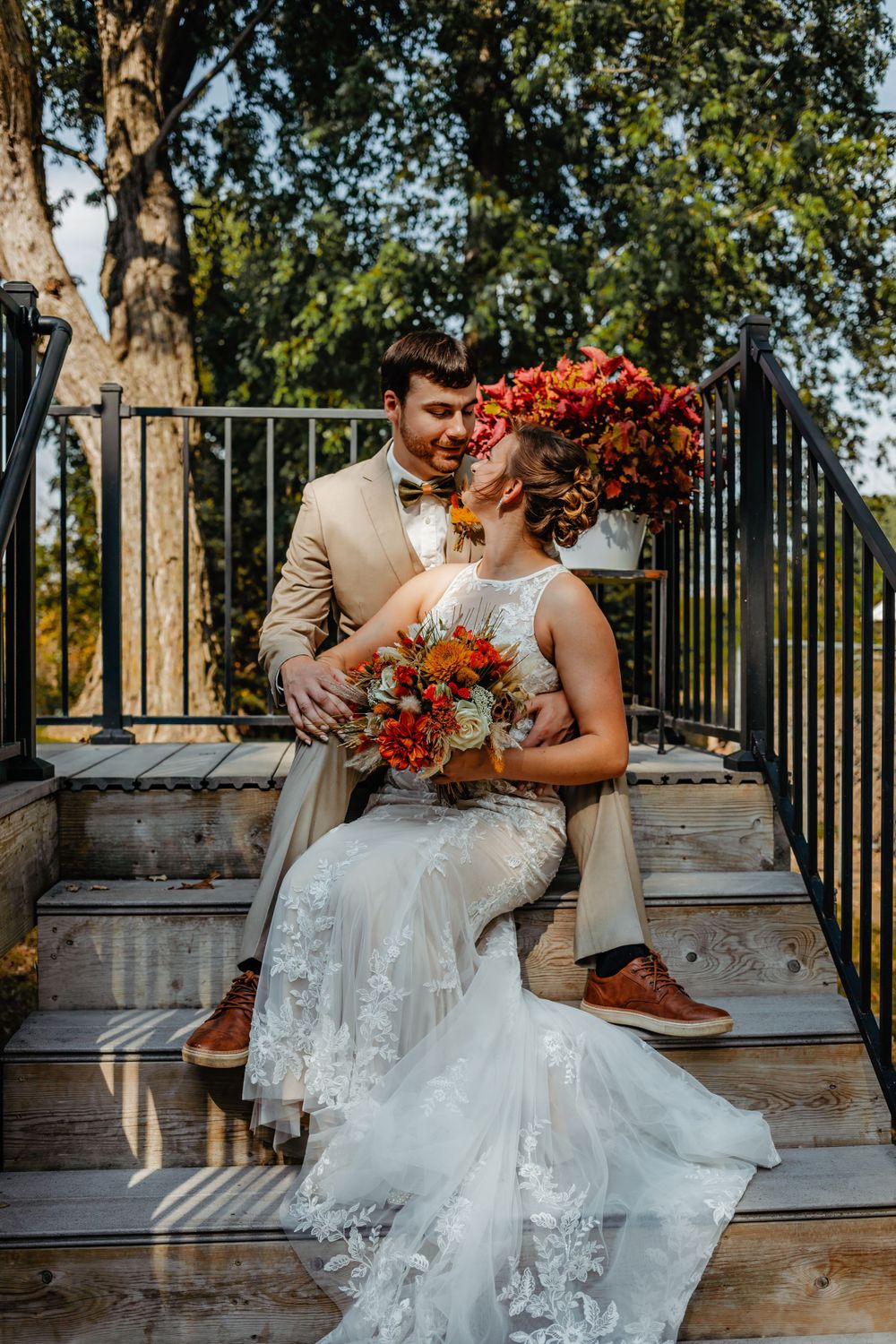 Couple in wedding attire posing on wooden steps with autumn florals.