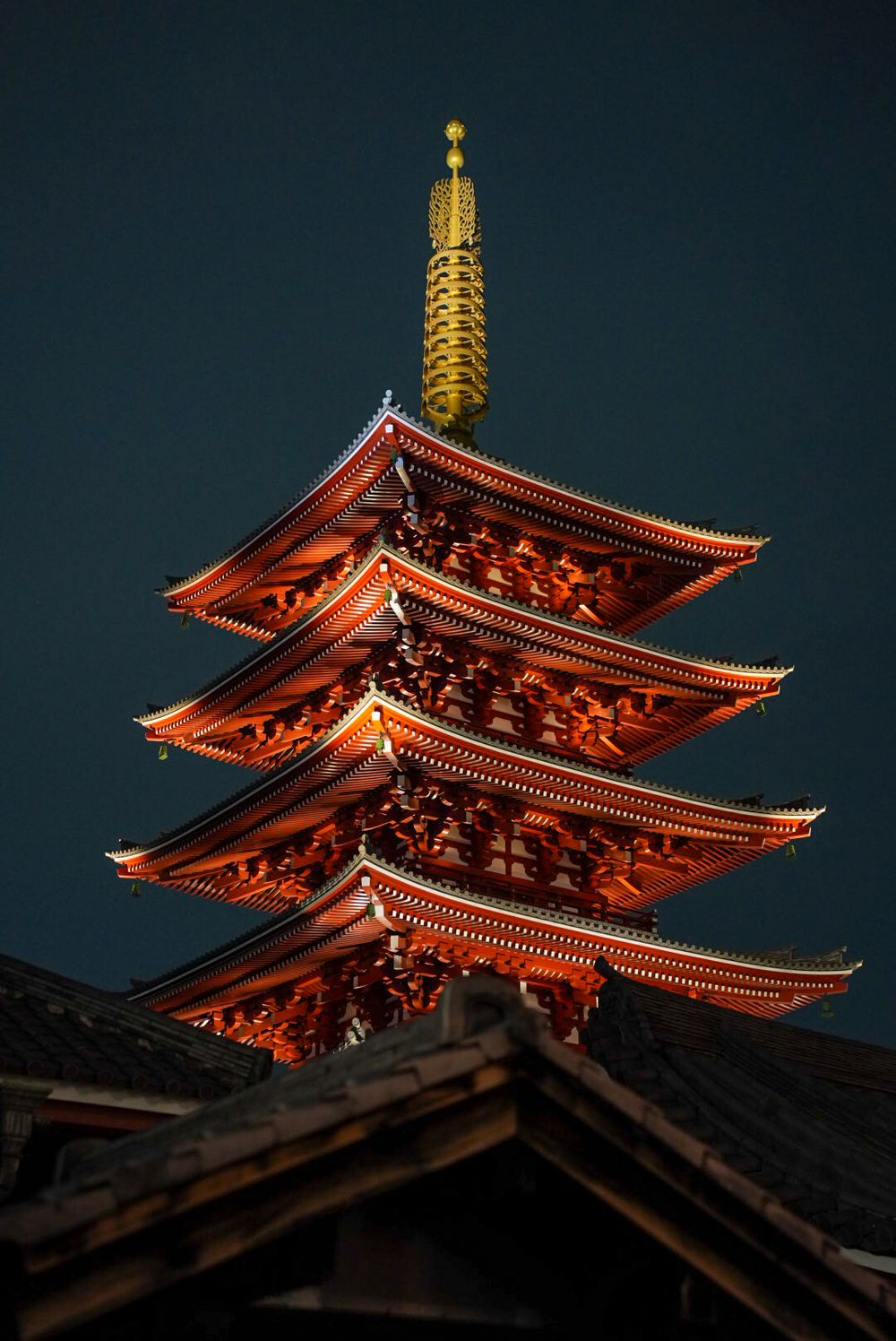 Illuminated traditional Japanese pagoda temple glowing red against dark night sky.