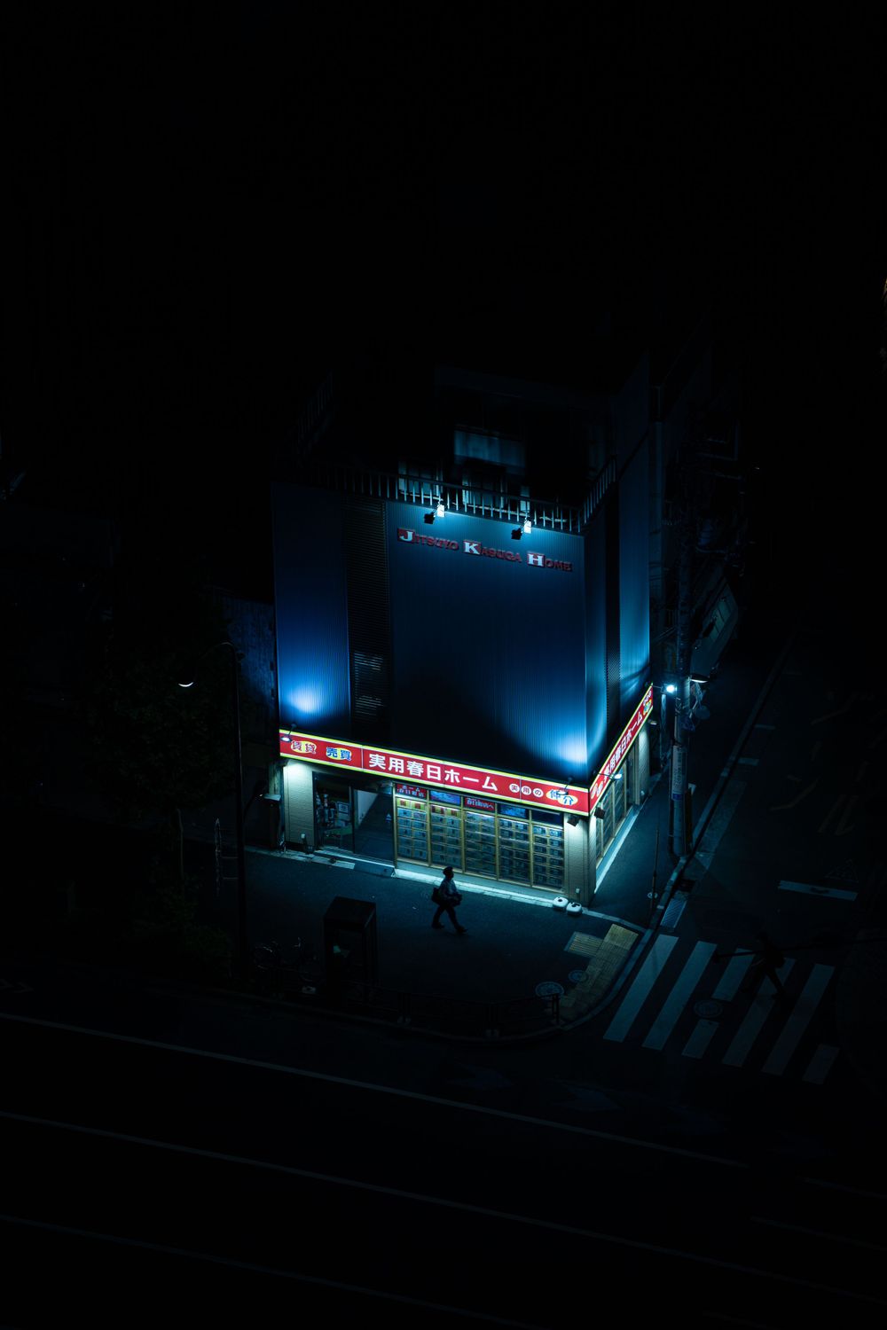 Blue-lit convenience store glowing in darkness on empty street corner.
