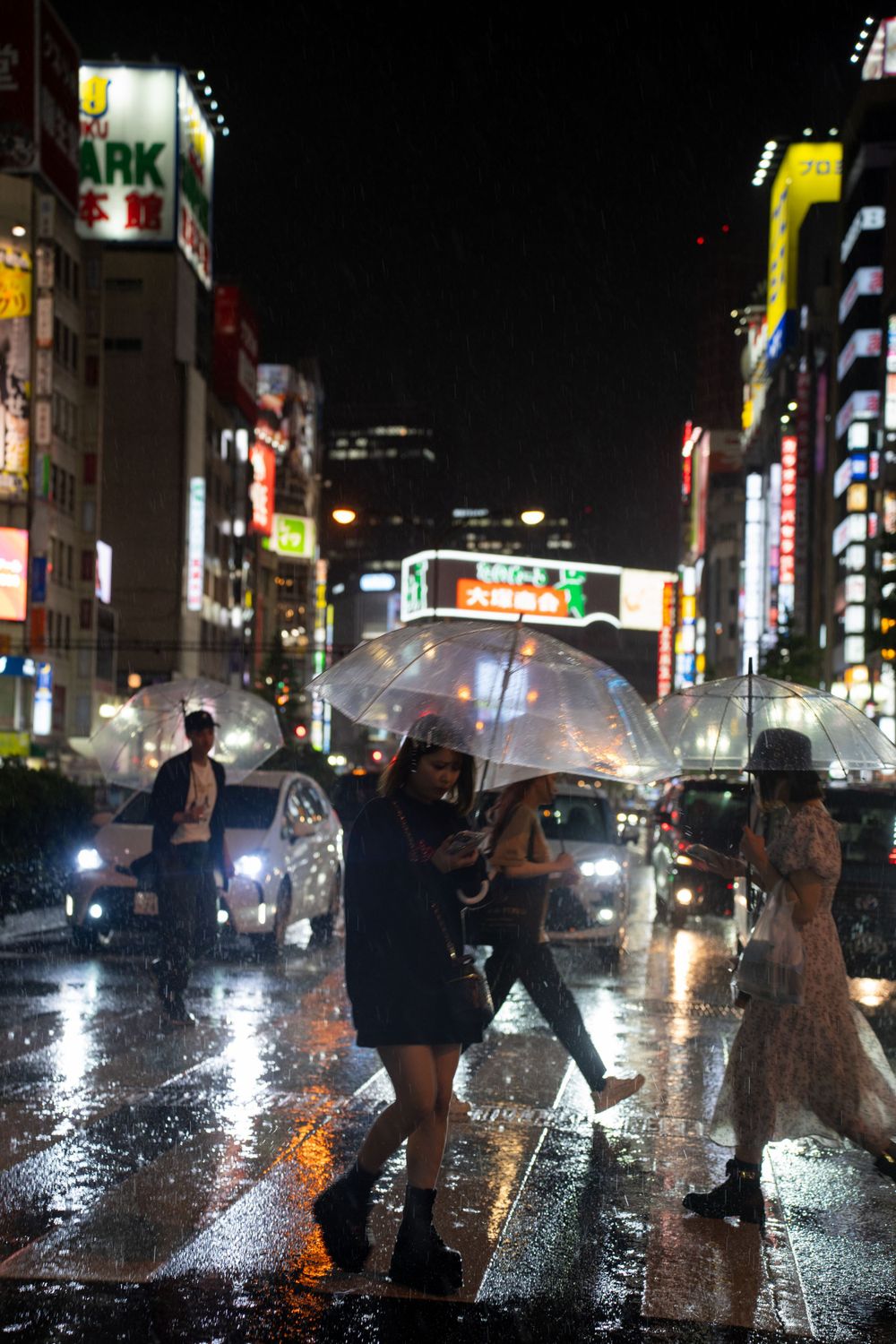 Rainy night scene in Tokyo with neon lights illuminating pedestrians with umbrellas.