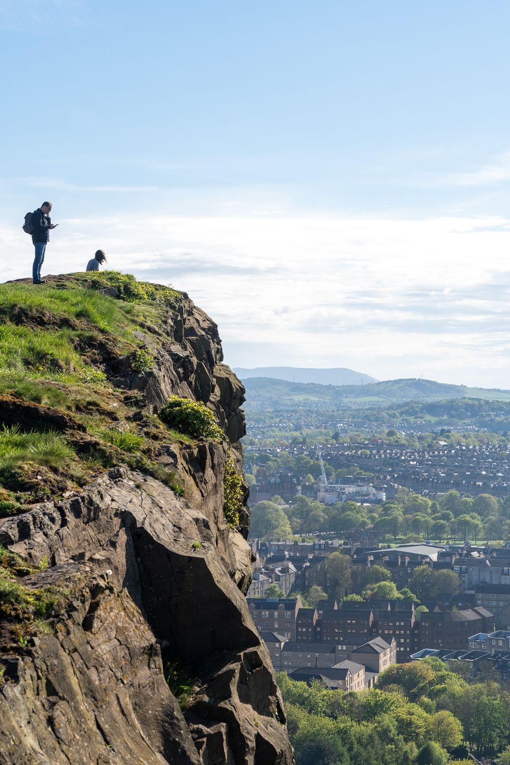 Scenic city view from atop Salisbury Crags in Edinburgh with dramatic cliffs in the foreground.