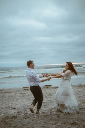 A couple dances playfully on the beach at dusk.