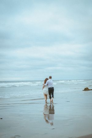 A couple walks together in the shallow ocean waves on a misty beach.