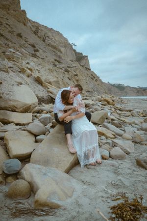 A tender embrace shared on rocky coastal cliffs under cloudy skies.