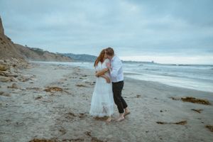 A romantic embrace on a cloudy beach with cliffs in the background.