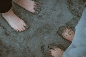 Bare feet walk along wet sand on a beach at sunset.
