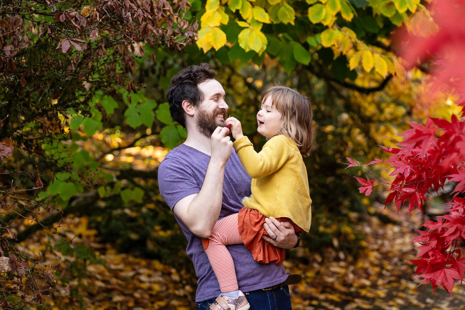 Father and daughter tickle each other with leaves in Seattle.